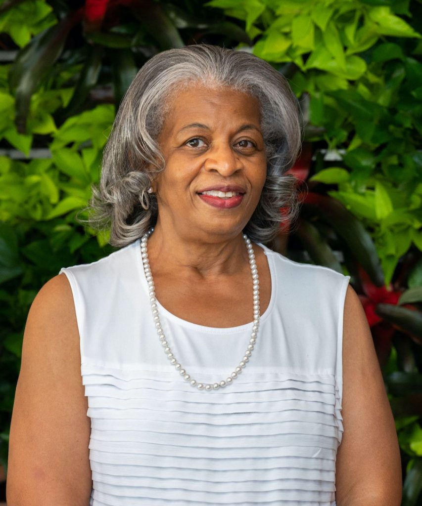 female with sleeveless white blouse in front a background of plants