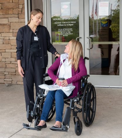 female patient in a wheelchair looking and speaking to a female nurse