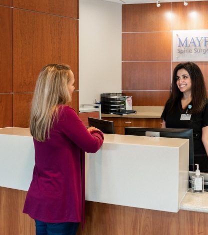 a female patient asking a female nurse at the front desk how to prepare for spine surgery